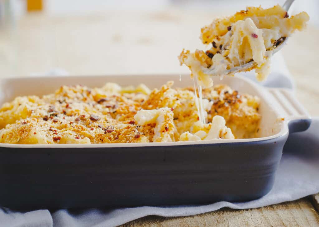 Baked Bacon Mac and Cheese with Bacon Crumb Topping being spooned out of disk