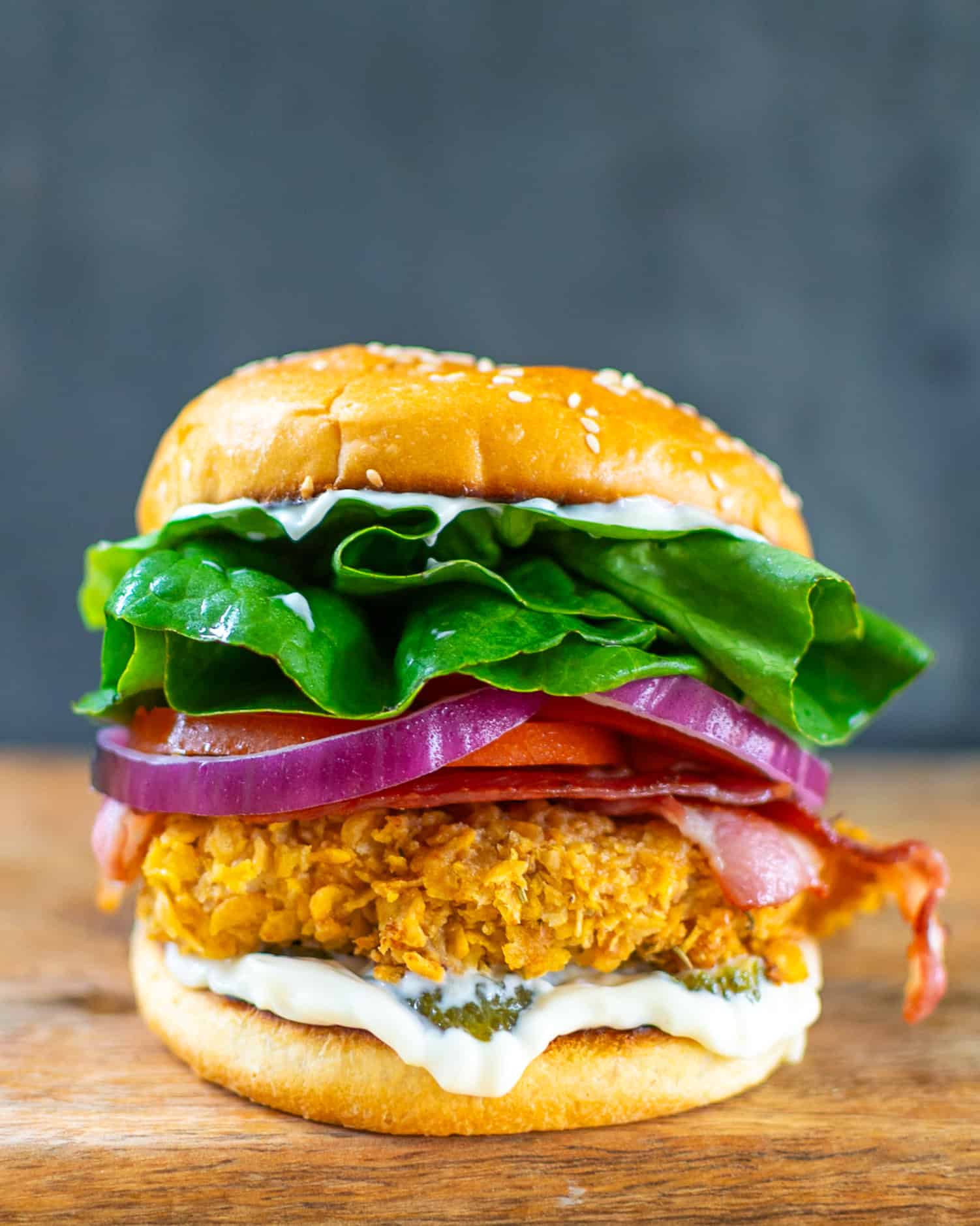 Crispy cornflake-crusted chicken sandwich on a sesame bun with lettuce, tomato, red onion and bacon.
