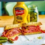 smoked meat sandwich on rye bread and mustard, a dill pickle on the side. Behind is a second half of a sandwich