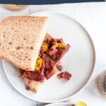 Top down photo of montreal smoked meat sandwich on rye bread and mustard, a dill pickle on the side.