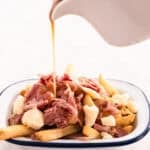 gravy being poured onto a plate of french fries and cheese curds and Montreal smoked meat