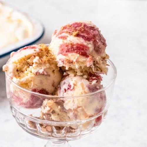 Scoop of rhubarb and custard ice cream topped with toasted oat crisp in a glass dessert dish.