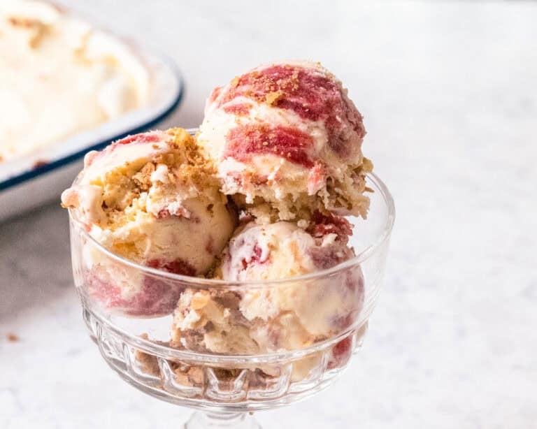 Scoop of rhubarb and custard ice cream topped with toasted oat crisp in a glass dessert dish.