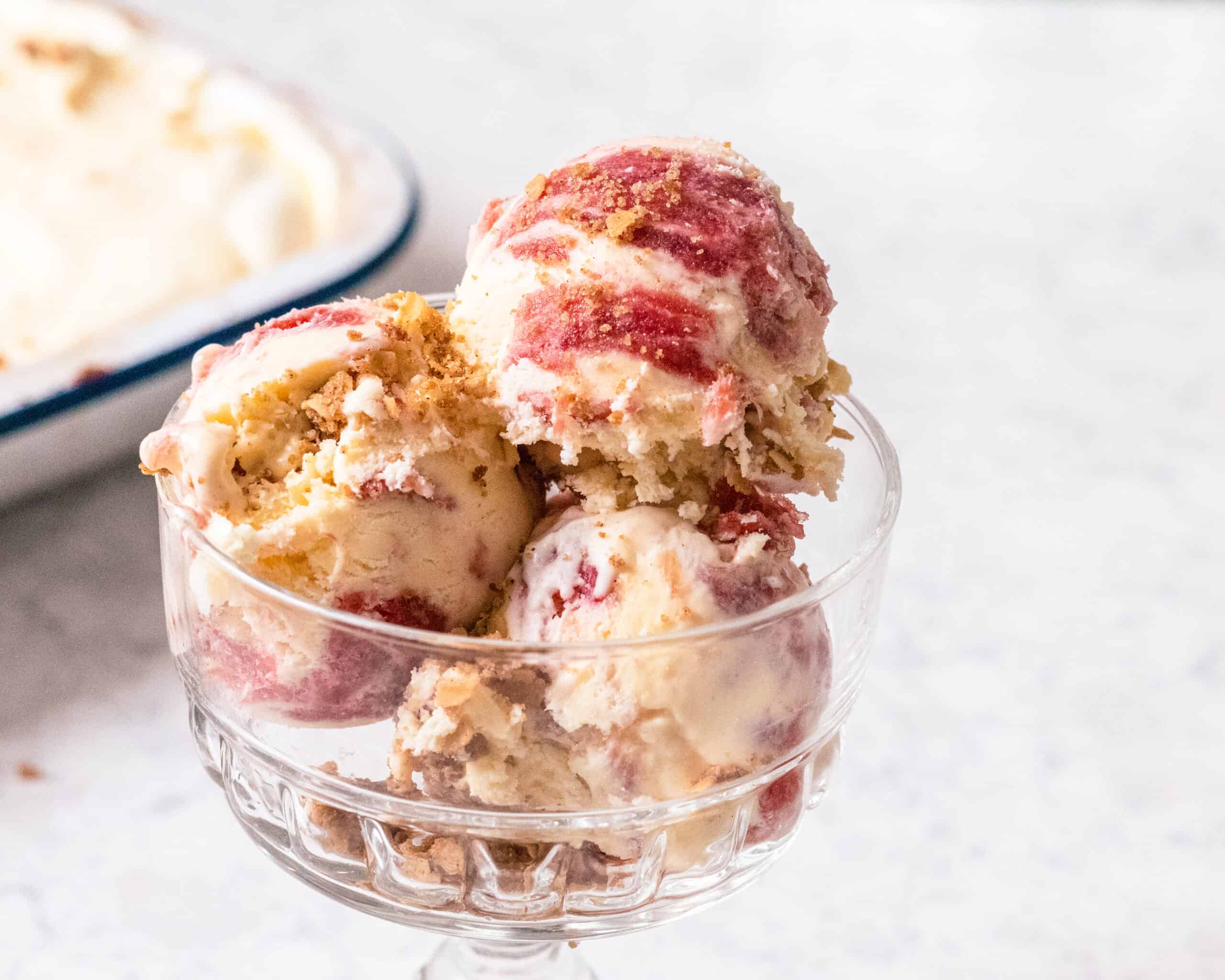 Scoop of rhubarb and custard ice cream topped with toasted oat crisp in a glass dessert dish.