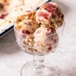 Scoop of rhubarb and custard ice cream topped with toasted oat crisp in a glass dessert dish.