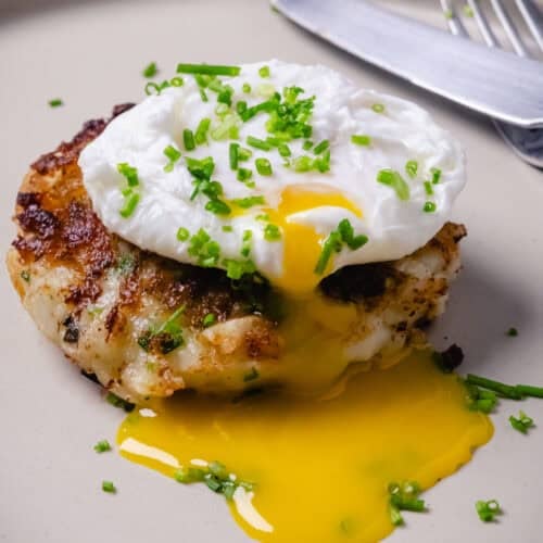 Golden Nova Scotia fish cakes with smoked haddock served with a poached egg on a cream plate.