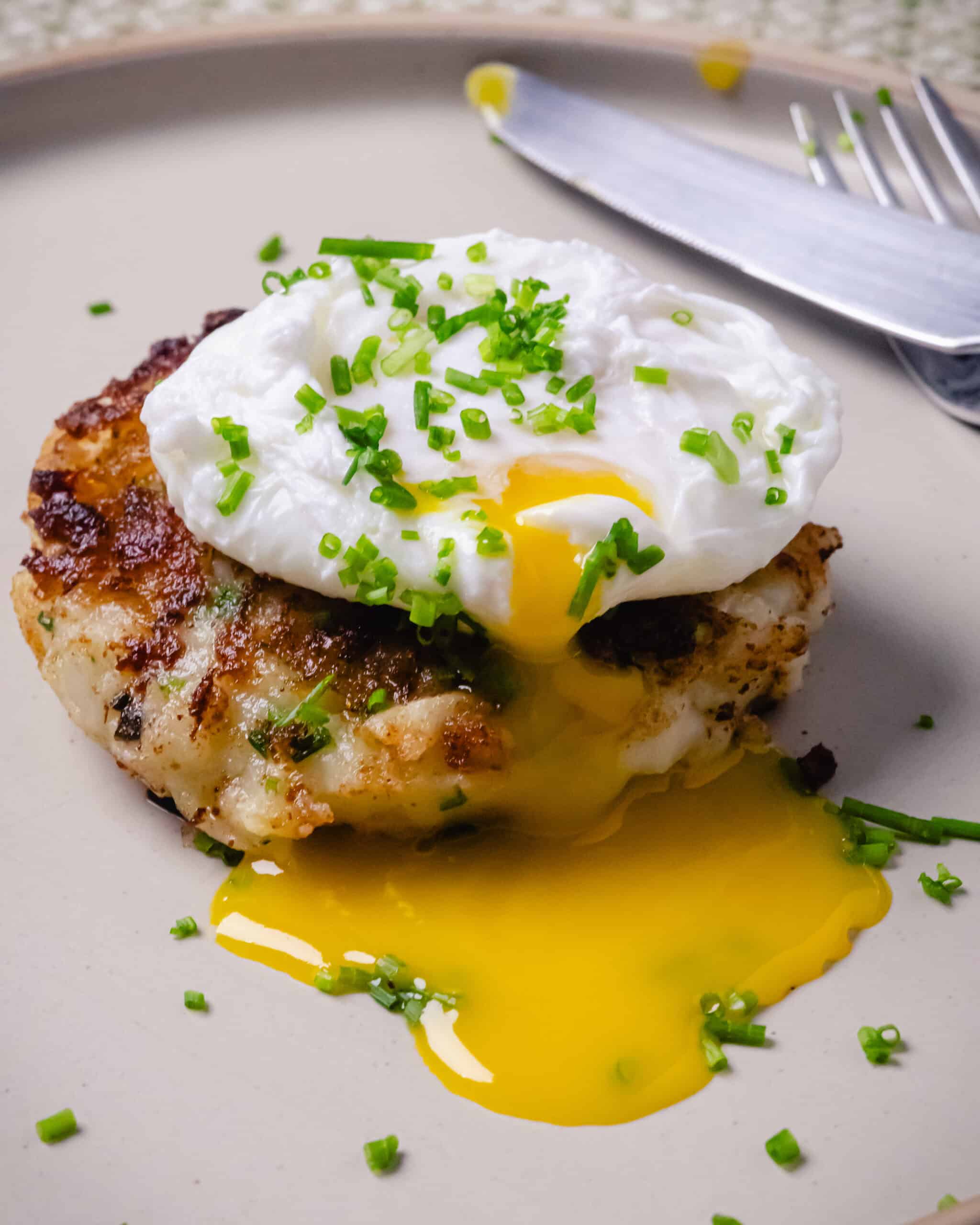 Golden Nova Scotia fish cakes with smoked haddock served with a poached egg on a cream plate.